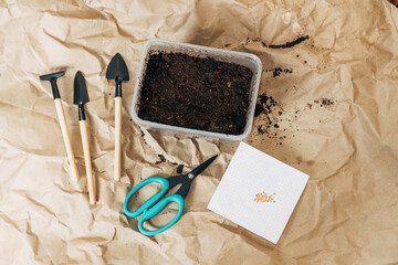 Kraft paper background, fertile soil and garden tools on top, top view. Planting seedlings in spring