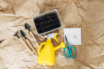 Kraft paper background, fertile soil and garden tools on top, top view. Planting seedlings in spring