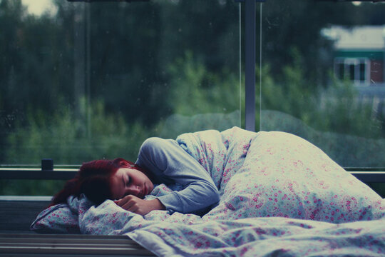 Close-up of a young woman sleeping under a duvet at a bus shelter