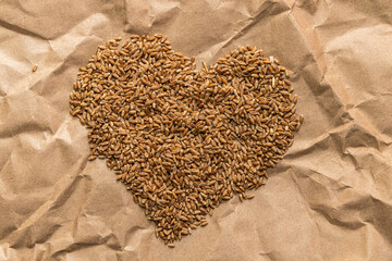 Golden wheat grains in the shape of a heart lie on a background of craft paper