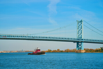 tugboat sails under a large bridge