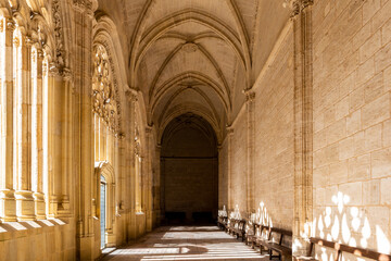 Obraz premium Cloister of the Segovia Cathedral in Spain, in Gothic flamboyant style with carved decorative vaults, columns and openwork tracery windows, sunlight coming in, creating shadows.