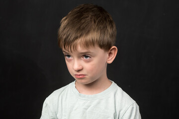A child with short brown hair and a light shirt is photographed against a dark backdrop. The...