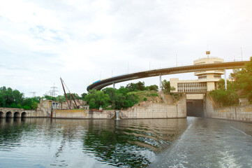 A modern hydroelectric dam with a curved bridge and control building, surrounded by lush greenery, reflecting in the calm water below. Ideal for energy, infrastructure, and engineering themes