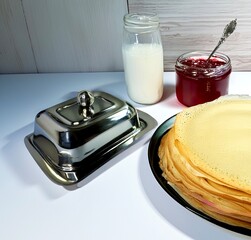 There is an iron Maslenitsa on the table, next to it there is a plate with pancakes, milk and jam.