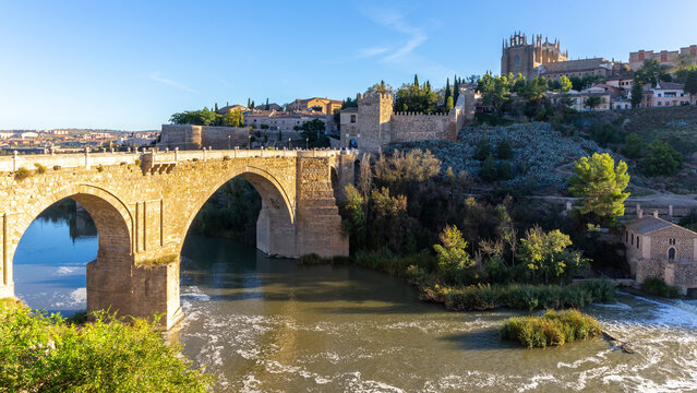 The San Martin Bridge, medieval bridge over the Tagus River with crenellated towers and Monastery of San Juan de los Reyes in the background, Toledo, Spain.