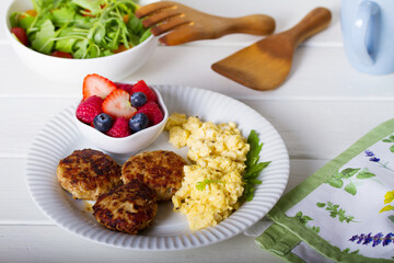 Turkey burgers with scrambled eggs and berries on white wooden background
