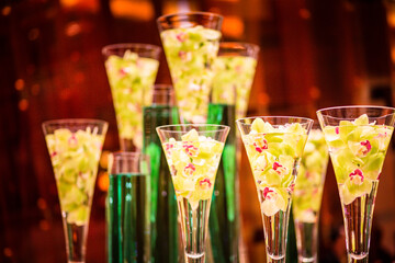 A row of green and clear glasses with flowers in them