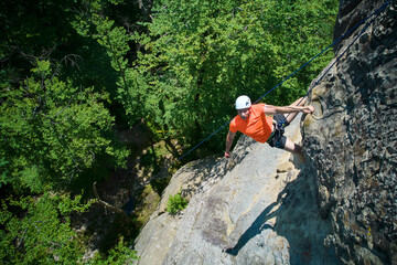 Aerial view of male rock climber ascending rugged limestone cliff with harness and rope for safety....