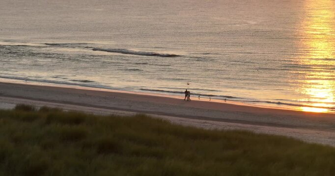 aerial view on couple having romantic beach walk at golden hour sunset.