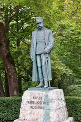 Obraz premium Innsbruck, Austria - September 30 2024: Bronze Statue of Emperor Franz Joseph I in Military Uniform and Overcoat, Set Against Green Trees in Park