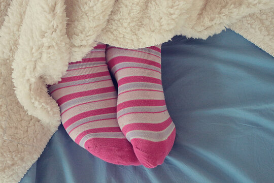 Overhead view of a woman's feet in pink striped socks sticking out from under a blanket