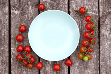 red cherry tomatoes on a wooden table around the empty plate