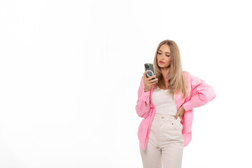 Young woman in pink jacket checking her phone while standing against a white background in a casual...