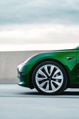 Fototapeta na wymiar Modern electric car with muted green bodywork and grey wheels parked on sleek pavement under overcast sky
