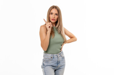 A woman poses with a finger pointing up, wearing a green top and light jeans, against a plain white...
