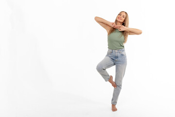 A joyful young woman dancing gracefully on one leg in casual attire against a white backdrop