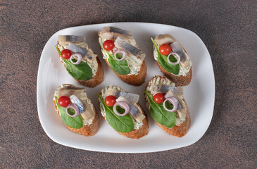 Bruschetta with herring, cream cheese, spinach and cherry tomatoes on white plate