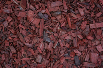 A layer of red wood mulch evenly spread out, featuring a texture of various shapes and sizes of wood chips. The photo conveys a natural decorative feel.