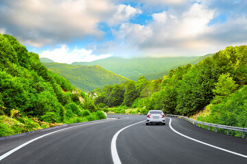 White car driving on nature road between green mountains in summer. Nature landscape on highway for...