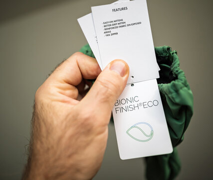 Paris, France - Dec 1, 2024: Close-up of a hand holding a product tag showcasing eco-friendly mittens with features like reinforced fabric, YKK zipper, and a Bionic Finish Eco label.