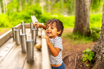 Curious toddler playing with metal cylinders on wooden table in park
