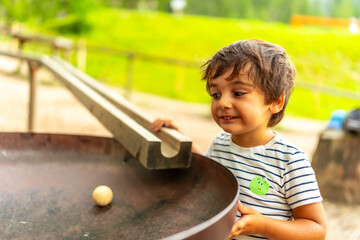 Child playing with wooden ball and track in playground, discovering gravity