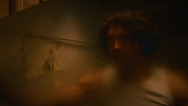 Mirror reflection shot of gen Y Caucasian man in undershirt wiping matted mirror and looking at himself in bathroom in evening, questioning meaning of life, depersonalization-derealization disorder