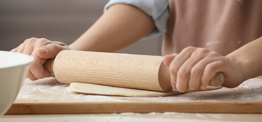 Woman rolling dough on kitchen table, closeup
