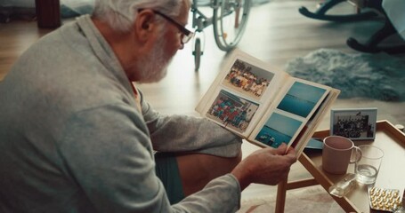 Grandfather reminisces about his youth by looking at an old photo album with photos from his past - Powered by Adobe