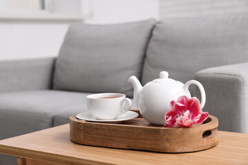 Teapot and cup of hot tea with tulip flower on table in living room