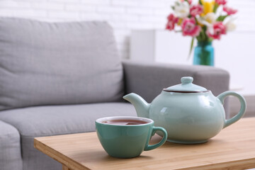 Teapot and cup of hot tea on table in living room