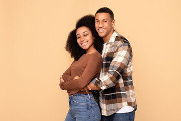 Happy African American spouses embracing warmly, sharing moment of closeness and affection, standing closely and smiling, beige studio background