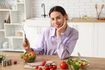 Beautiful young woman with glass bowls of fresh vegetable salad at table in kitchen