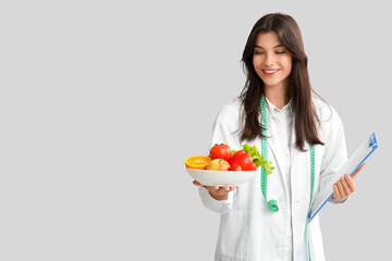 Female nutritionist with healthy food and clipboard on light background