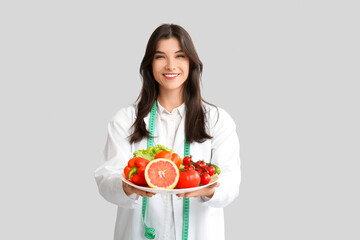 Female nutritionist with healthy food on light background