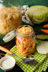 Tasty sauerkraut in jars with ingredients on green background