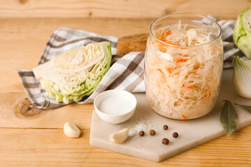 Delicious sauerkraut in jar with ingredients on wooden background
