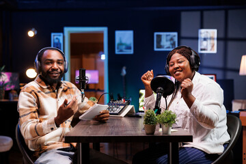During talk show, male host interviews excited female blogger using professional recording equipment. Together, they create engaging creative content for their online audience.