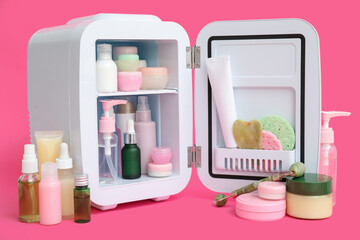 Small cosmetic refrigerator with cosmetic products on pink background