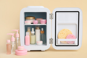 Small cosmetic refrigerator with cosmetic products on beige background