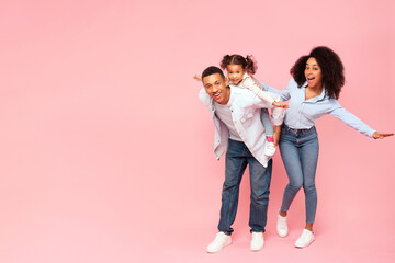 Fototapeta premium Full body length of funny black family of three posing on pink studio background, man piggybacking daughter, carrying girl on back, free space