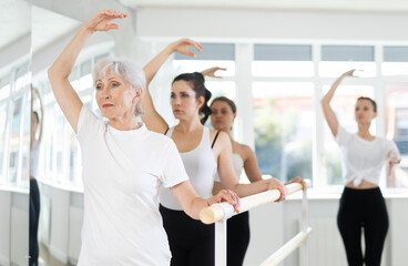 Obraz premium Adult female trainer teaching group of women to perform ballet movements in studio