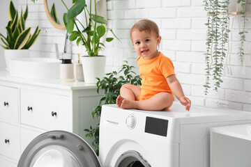 Cute little baby sitting on washing machine in laundry room