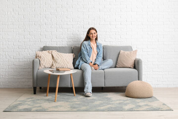 Young beautiful woman resting on grey sofa at home