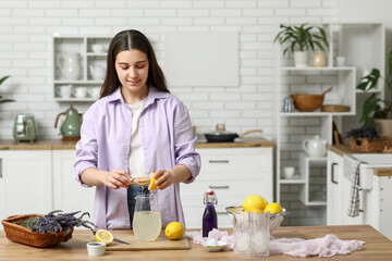 Young woman squeezing lemon for preparing lavender lemonade at table in kitchen