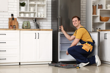 Happy male worker with tools repairing refrigerator in kitchen