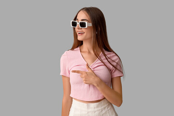 Young woman in sunglasses with diastema pointing at something on light background