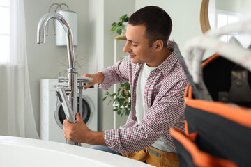 Male plumber fixing bathtub faucet in bathroom