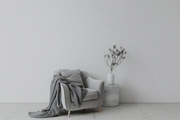 A grey armchair with a throw blanket and a vase of dried flowers on a side table in a white room